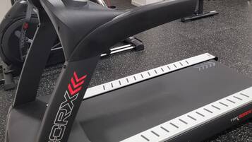 Un vélo d’appartement, un banc et un appareil de musculation dans une salle de sport.