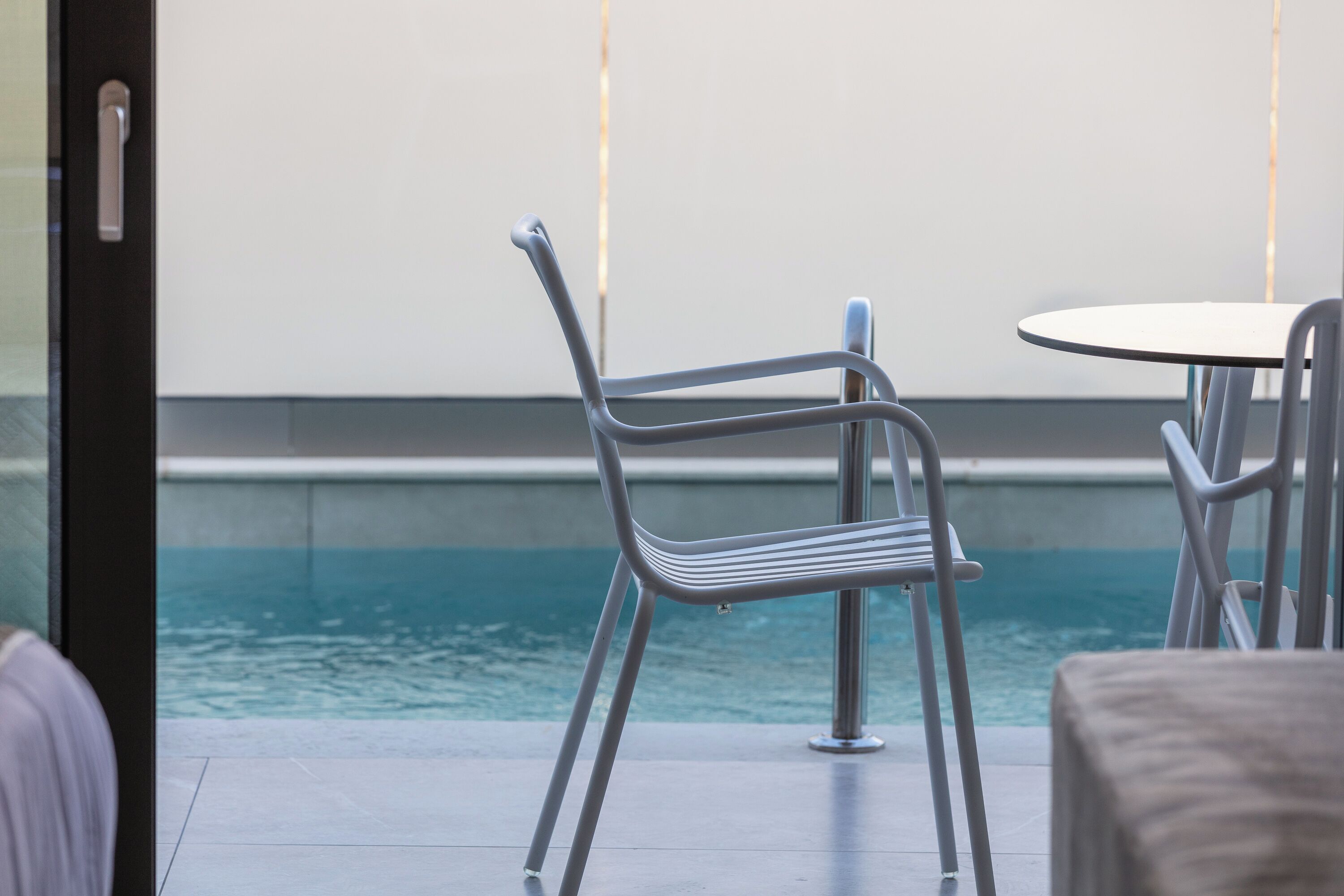 A modern outdoor seating area with metal chairs and a round table, overlooking a pool.