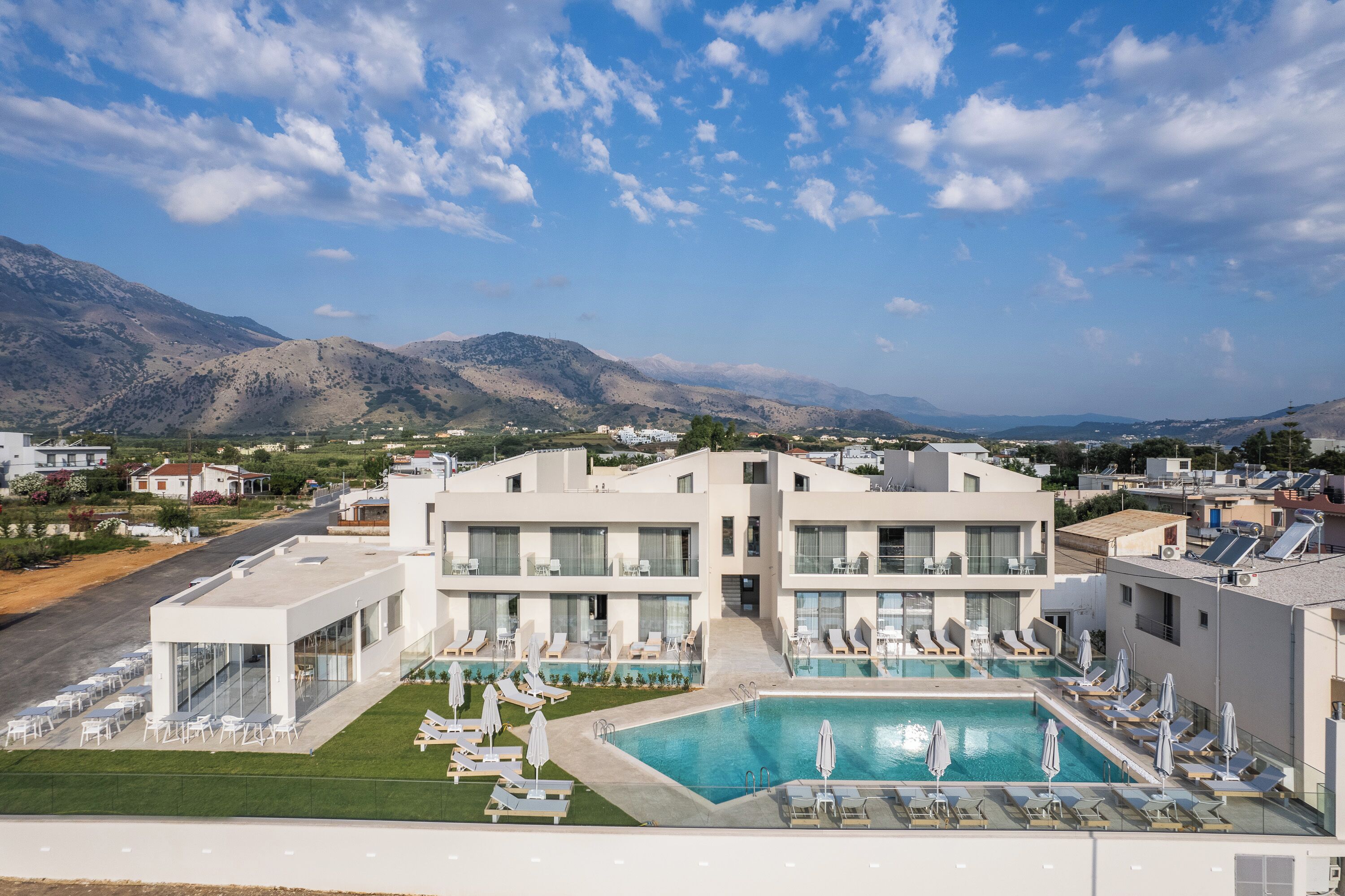 A modern hotel with a rooftop pool, lounge chairs, and a view of mountains.