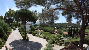 A pathway leading through a garden with trees and shrubs, surrounded by residential buildings. - Hotel Villa Giulia (Porto Azzurro)