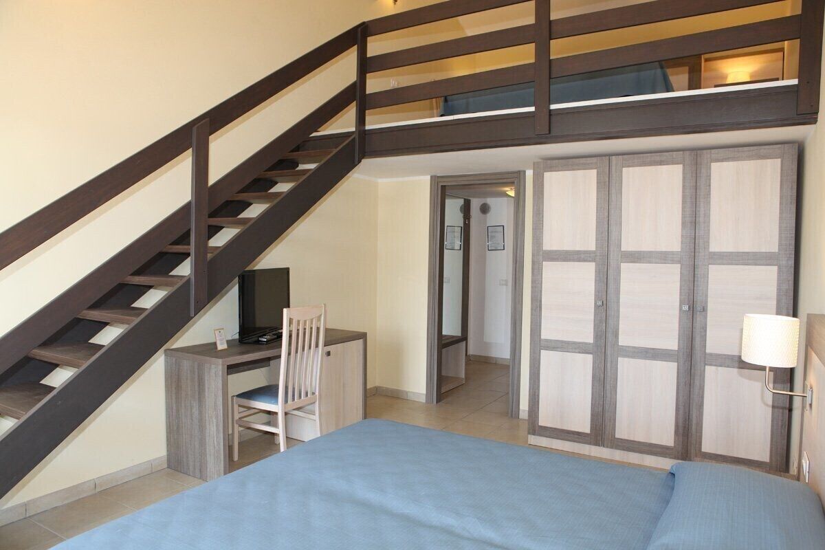 A bedroom with a bed, a desk with a chair, a TV, and a wardrobe.