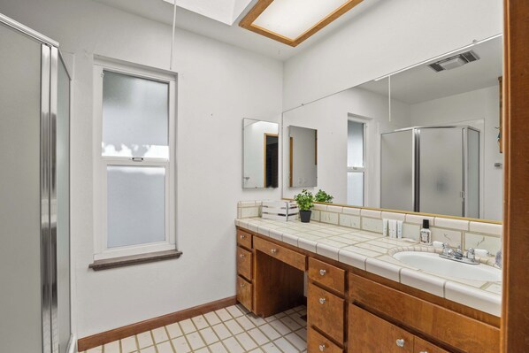 A modern bathroom with a large mirror, wooden cabinets, a sink, and a window.