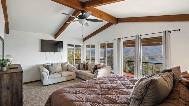 Ein Schlafzimmer mit einem großen Bett, einem Deckenventilator, einem Fernseher und einem Balkon mit Bergblick.