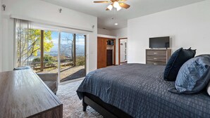 Ein Schlafzimmer mit Bett, Fernseher, Deckenventilator und Blick durch die Glastür.