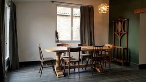 Un coin repas avec une table et des chaises en bois, une fenêtre avec des rideaux et un luminaire suspendu.