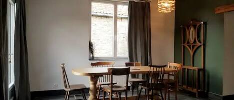 A dining area with a wooden table and chairs, a window with curtains, and a hanging light fixture.