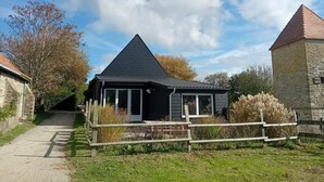 Un bâtiment noir avec un toit triangulaire, une tour en pierre et une clôture en bois, situé dans un cadre rural.