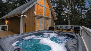 A hot tub with a wooden deck, a wooden cabin with large windows, and a deck chair. - Hot Tub, Fire Pit, Deck, Grill, WiFi, Dog-Friendly (Gerrardstown)