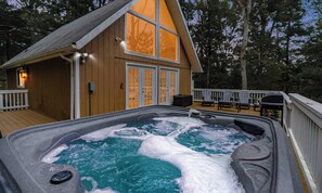 A hot tub with a wooden deck, a wooden cabin with large windows, and a deck chair. - Hot Tub, Fire Pit, Deck, Grill, WiFi, Dog-Friendly (Gerrardstown)