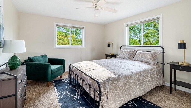 A bedroom with a bed, two windows, a ceiling fan, a green armchair, a dresser, and a nightstand with a lamp. - Hot Tub, Fire Pit, Deck, Grill, WiFi, Dog-Friendly (Gerrardstown)