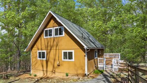 A two-story wooden house with a gabled roof, a front porch with a white railing, and a gravel driveway. - Hot Tub, Fire Pit, Deck, Grill, WiFi, Dog-Friendly (Gerrardstown)