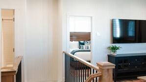 Un interior moderno con una escalera, una cama con ropa de cama azul, un mueble de madera oscura y un televisor de pantalla plana montado en la pared.