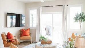 Una sala de estar moderna con un sofá, sillones, un televisor y un ventanal con cortinas.