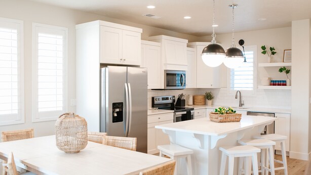 Una cocina moderna con armarios blancos, electrodomésticos de acero inoxidable y una isla central con taburetes de bar.