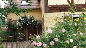 Una casa rústica con jardín, con rosales rosados y diversas plantas.