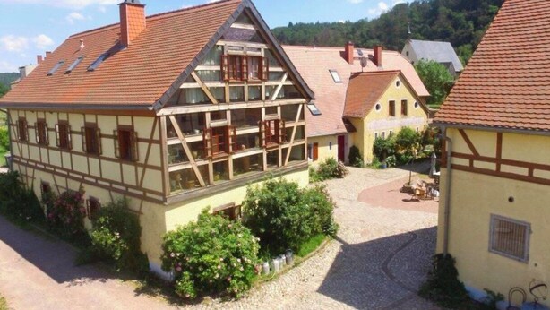Una casa tradicional de entramado de madera con tejado inclinado, un patio interior y vegetación circundante.