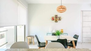 Un espace repas moderne avec une table blanche, des chaises noires et un luminaire suspendu.