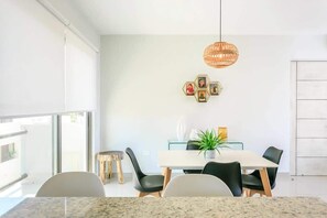 Un espace repas moderne avec une table blanche, des chaises noires et un luminaire suspendu.