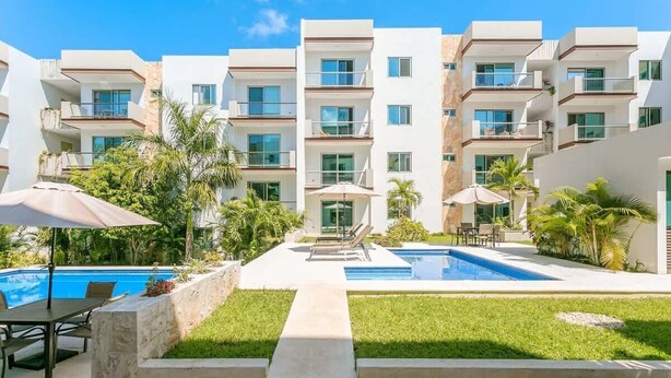 A modern hotel with a swimming pool, outdoor seating, and a well-maintained garden. - Spacious Retreat- Pool, Gym, 3 Balconies & Parking (Playa del Carmen)