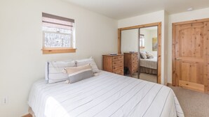 Un dormitorio con cama, cómoda, espejo y ventana con vistas a árboles.