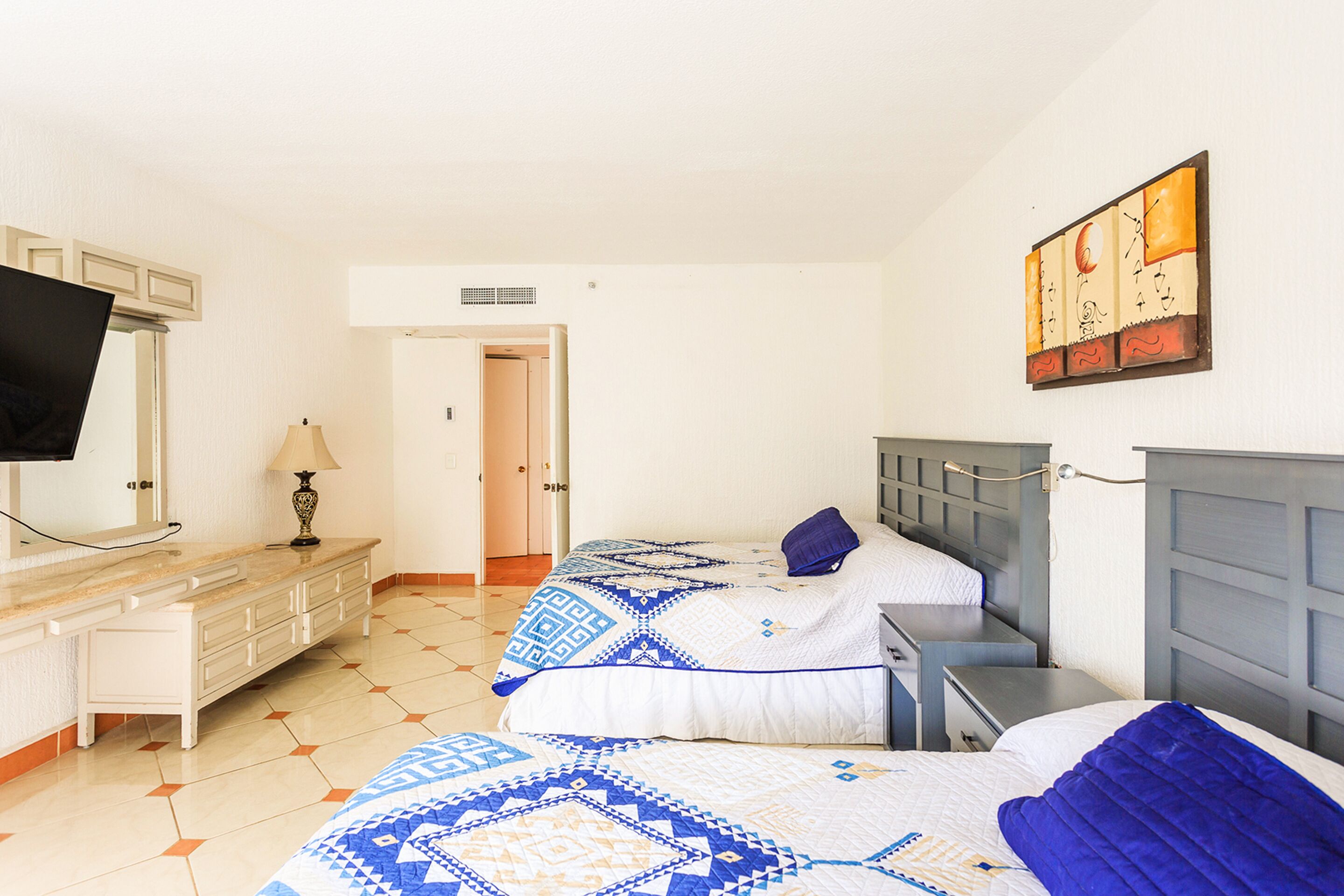Ein Hotelzimmer mit zwei Betten, einem Fernseher, einem Schreibtisch und einem Gemälde an der Wand.