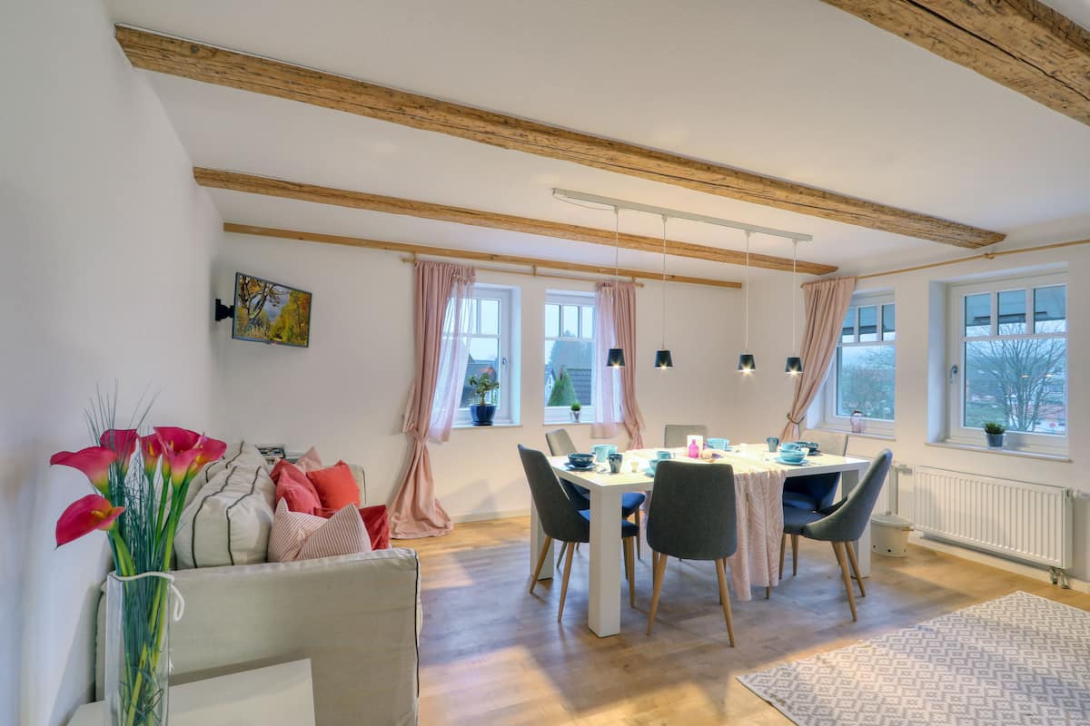 A dining area with a wooden ceiling, a table with chairs, and a vase of flowers.