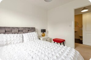 A bedroom with a bed, a nightstand, a lamp, and a red bench.