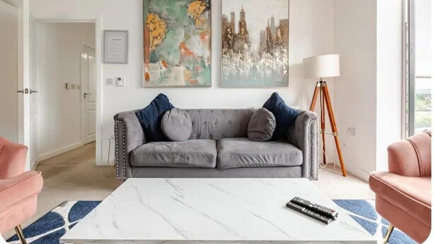 A living room with a grey sofa, a white coffee table, and two pink armchairs. There are two abstract paintings on the wall and a floor lamp. - Stunning Modern Apartment in Rochester, England (Rochester)