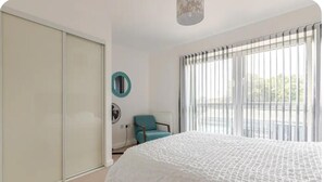 A bedroom with a bed, a chair, a wardrobe, and a window with blinds. - Stunning Modern Apartment in Rochester, England (Rochester)