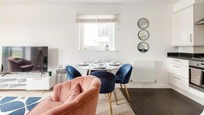 A modern living room with a TV, a pink armchair, and a dining area with a table set for four. - Stunning Modern Apartment in Rochester, England (Rochester)