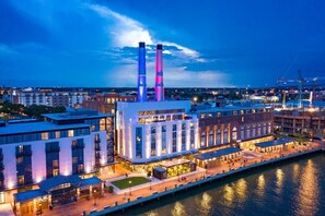 A waterfront hotel with two prominent towers, a riverside promenade, and a mix of modern and traditional architecture.