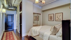 Ein Schlafzimmer mit einem Bett, einem Nachttisch, einer Kommode, einem Spiegel und gerahmten Bildern an der Wand.