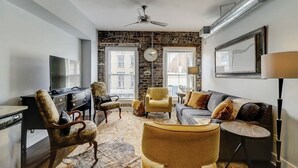 Ein modernes Wohnzimmer mit einer Wand aus Stein, einem Deckenventilator, einem Flachbildfernseher und einer Couch mit Kissen.