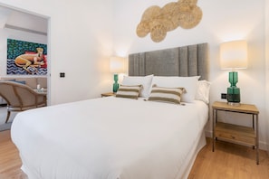 A neatly made bed with white linens, two bedside tables with green lamps, a grey headboard, and a wall art piece above the bed.