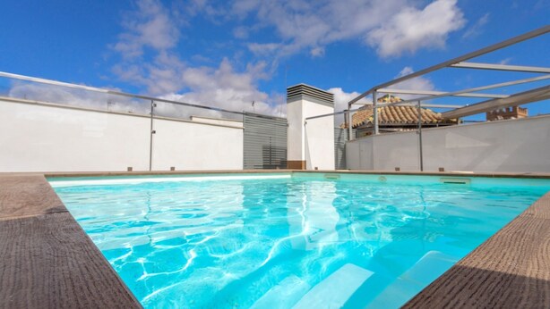 A rooftop swimming pool with clear blue water, surrounded by a white wall and a metal railing. - Genteel Home Goyeneta (Seville)