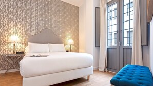 A bedroom with a bed, bedside lamps, a blue ottoman, and a patterned wall. - Genteel Home Goyeneta (Seville)