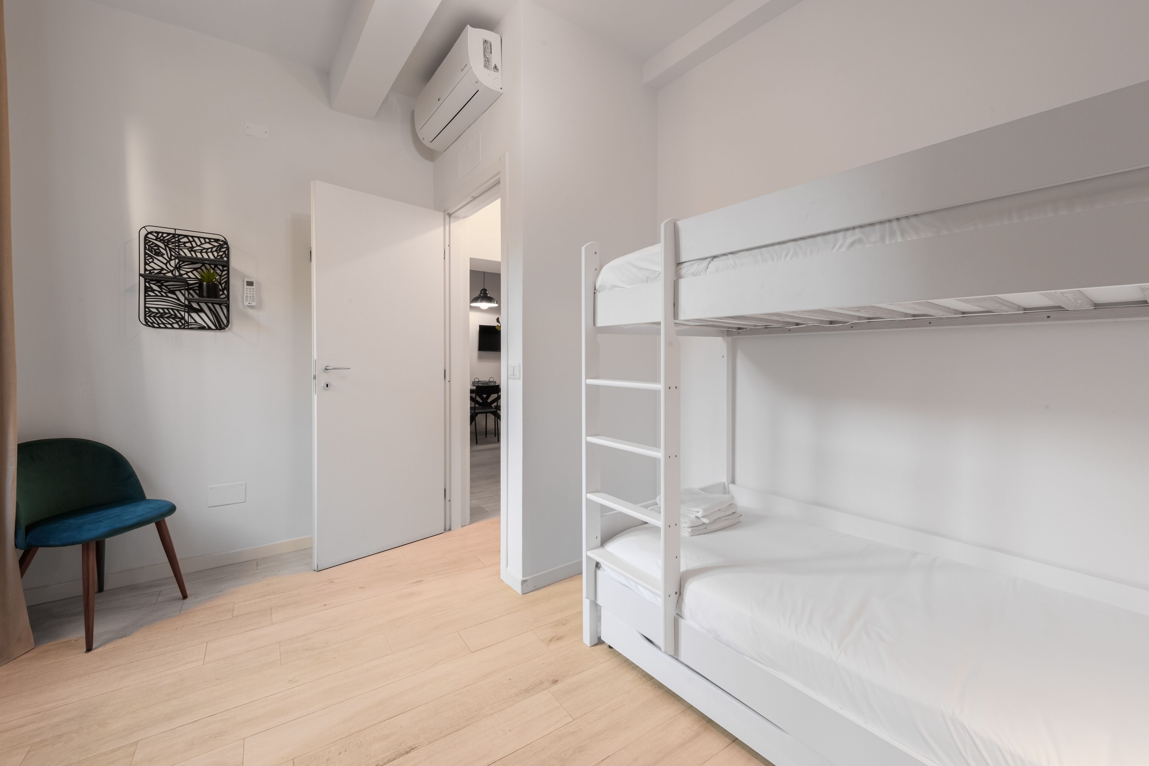 Una habitación con literas, una silla, aire acondicionado en la pared y una puerta que da a un armario.