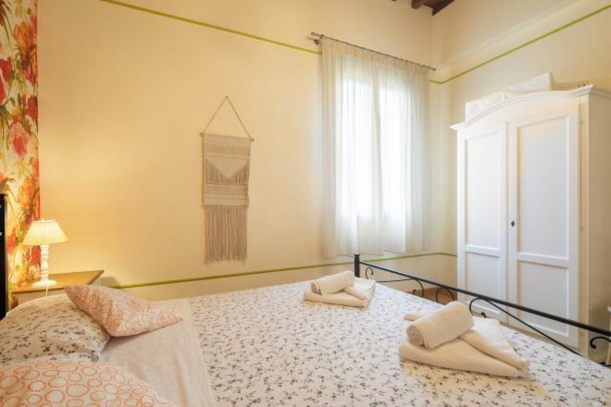 A bedroom with a bed, a hanging tapestry, a wardrobe, and a window with curtains.