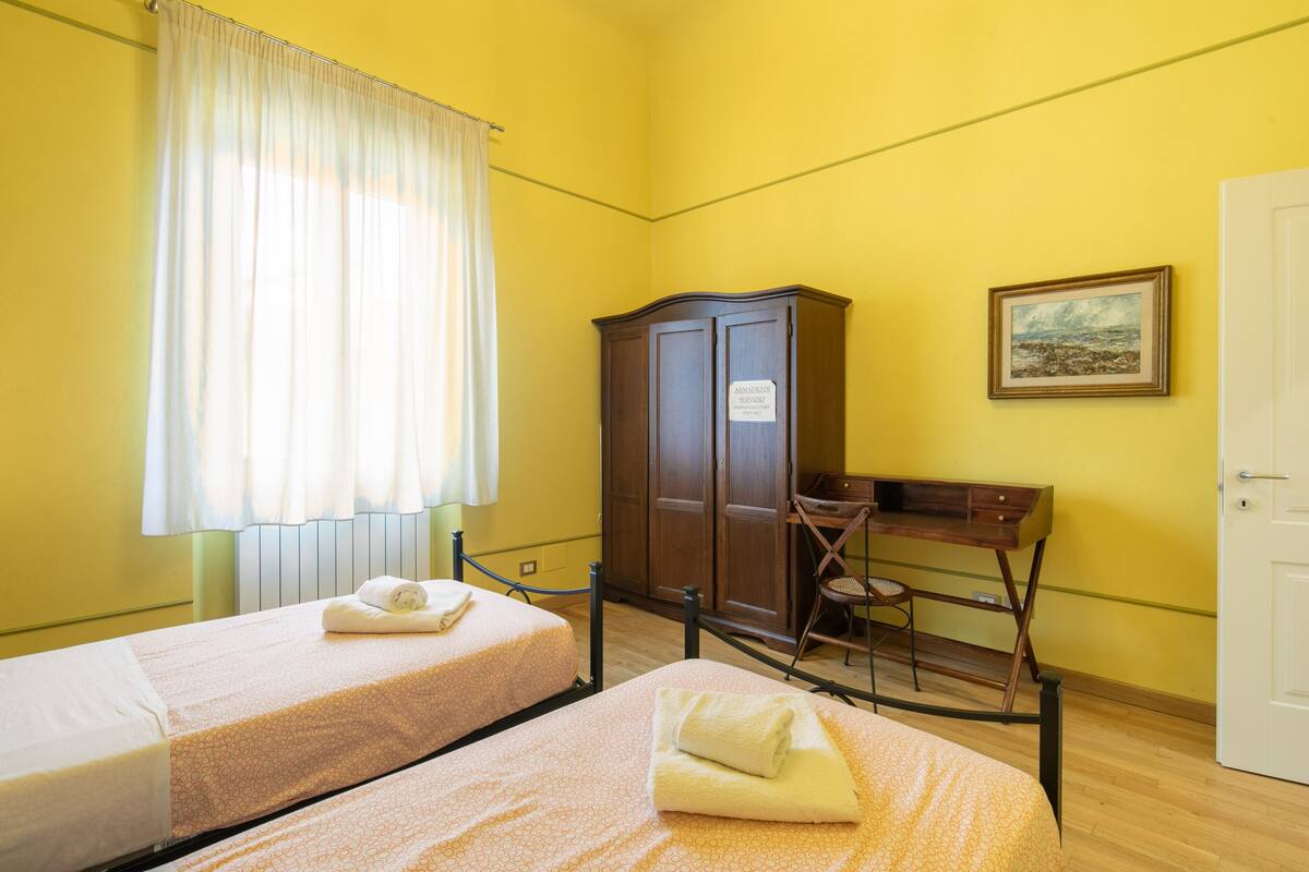 A room with two single beds, a wooden desk, a chair, a cabinet, and a painting on the wall.