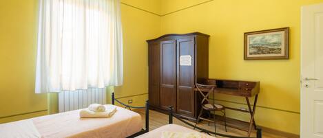 Una habitación con dos camas individuales, un escritorio de madera, una silla, un armario y un cuadro en la pared.