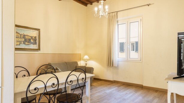 Un coin repas comprenant une table, des chaises, un canapé, un lustre et une fenêtre avec des rideaux.