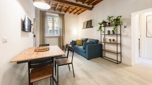Un salon moderne avec une table à manger en bois, un canapé bleu et une étagère en métal noir agrémentée de plantes.