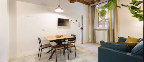 A modern living room with a wooden dining table, chairs, a blue sofa, and a hanging plant.