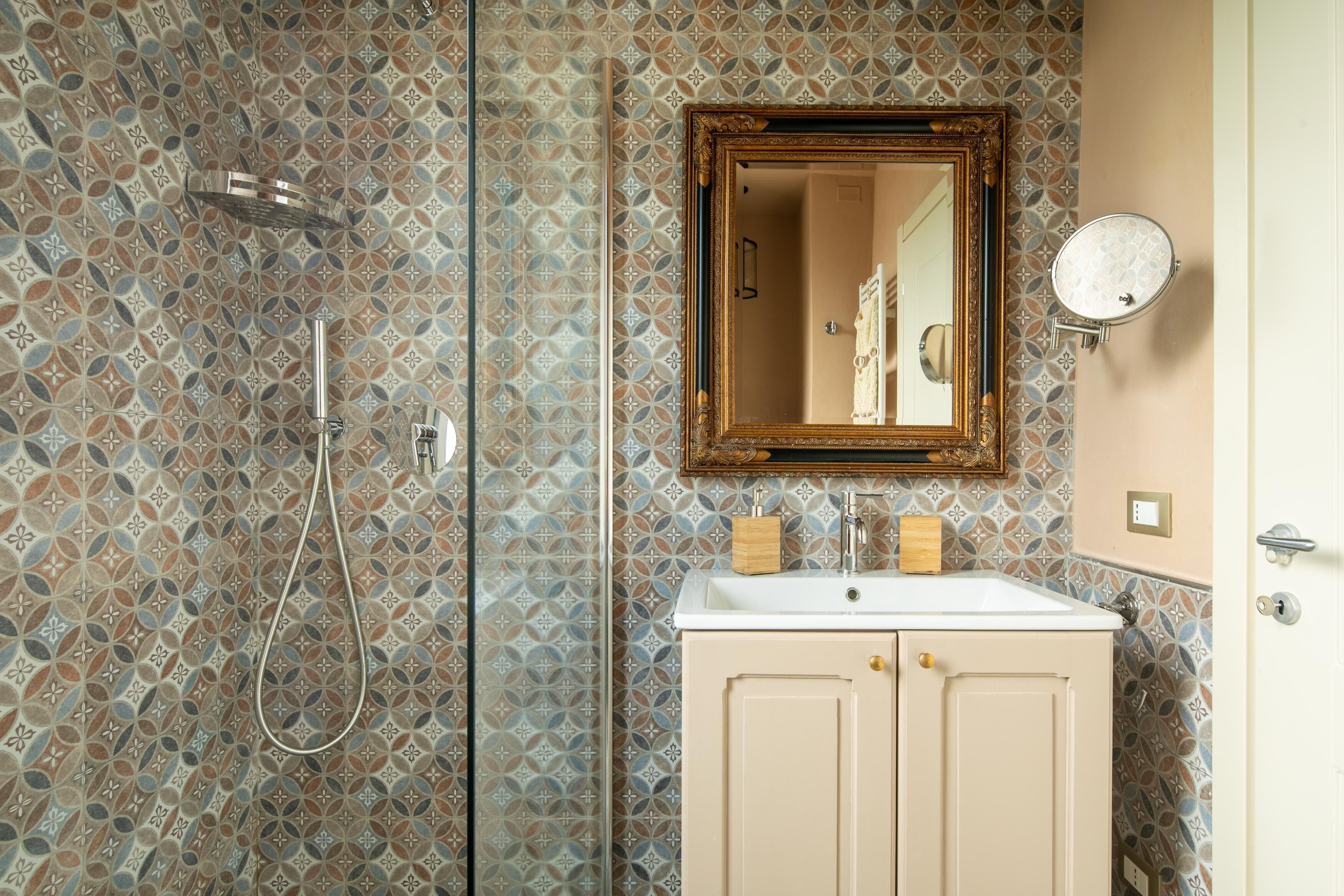 A bathroom with patterned tiles, a shower, a sink with a mirror, and a cabinet.