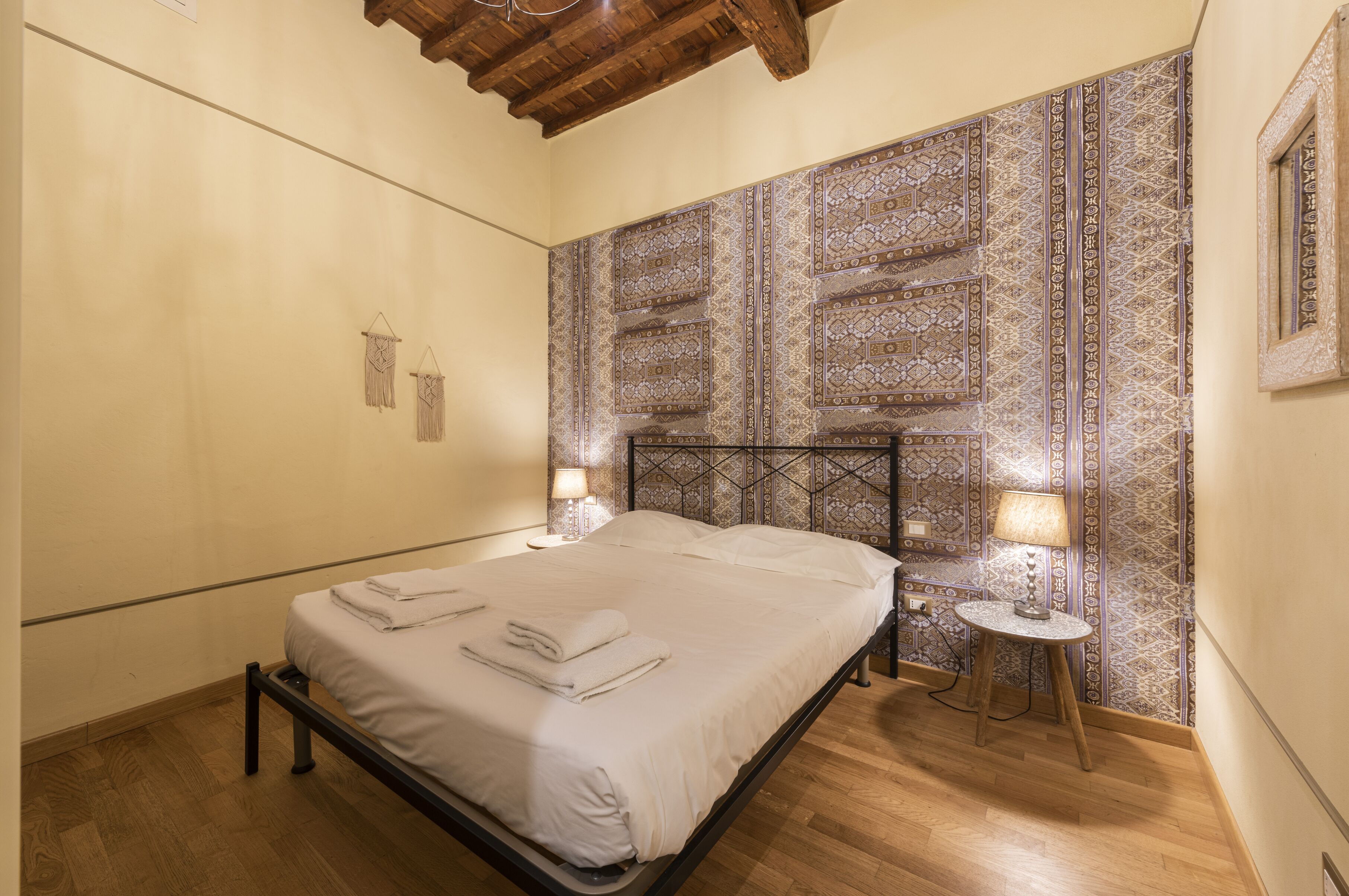 A bedroom with a bed, bedside lamps, and a patterned wall.