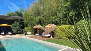 A swimming pool with clear water, surrounded by a wooden deck. There are lounge chairs and a thatched-roof structure in the background. - Charming gîte in wooded grounds with swimming pool, 30 minutes from Bordeaux (Civrac-de-Blaye)