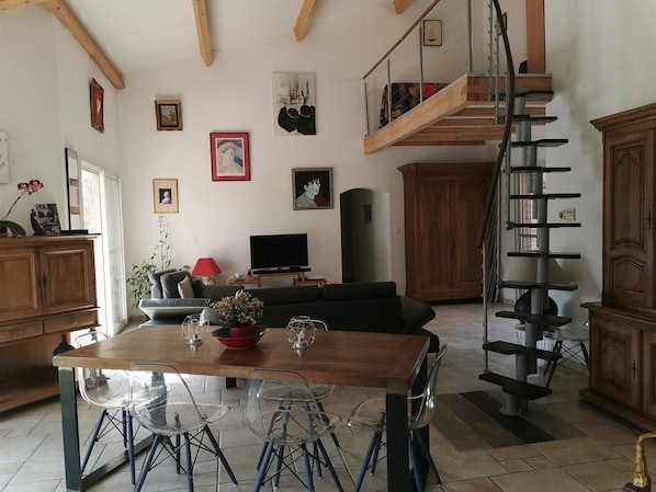 Un vaste espace de vie comprenant une table à manger en bois, des chaises transparentes, un canapé et un escalier.