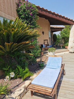 Une terrasse en bois avec un fauteuil de relaxation, entourée d’une végétation luxuriante et de plantes en pot.