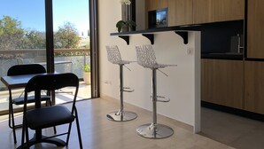 Una cucina moderna con mobili in legno, un piano di lavoro nero e una piccola TV. Sono presenti due sgabelli da bar con top in vetro e un tavolo da pranzo con sedie.