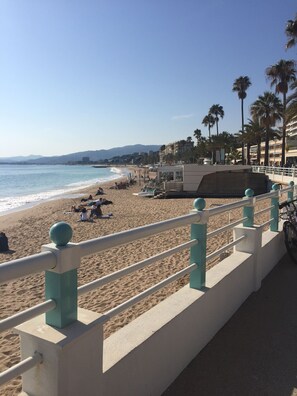 Une plage avec une balustrade blanche et turquoise, des palmiers et un ciel dégagé.